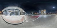 a fish - eye lens view of a parking lot and street corner at night with a man walking beside the road