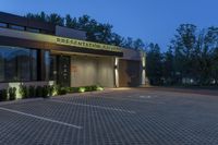 a photo taken at night of the front of a building at dusk with lights on and landscaping lighting up