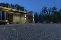 a photo taken at night of the front of a building at dusk with lights on and landscaping lighting up