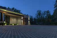 a photo taken at night of the front of a building at dusk with lights on and landscaping lighting up