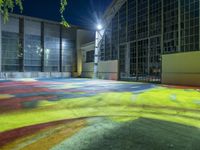 colorfully painted playground in front of large building at night, lit with streetlights