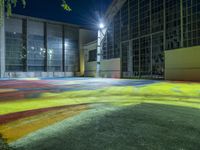 colorfully painted playground in front of large building at night, lit with streetlights