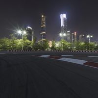 a large racetrack with buildings at night in the background with a few cars driving on it