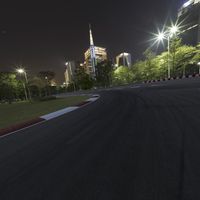 a large racetrack with buildings at night in the background with a few cars driving on it