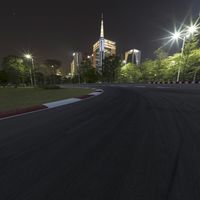 a large racetrack with buildings at night in the background with a few cars driving on it