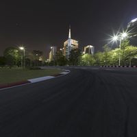 a large racetrack with buildings at night in the background with a few cars driving on it