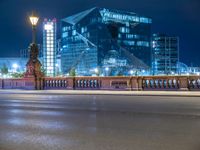 a woman riding her bike across a street next to a tall building at night on a city street