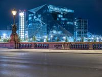 a woman riding her bike across a street next to a tall building at night on a city street