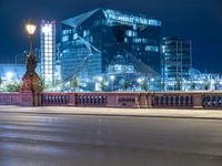 a woman riding her bike across a street next to a tall building at night on a city street