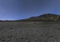 the stars are in the sky above a mountain and dirt area on the horizon are black rocks