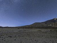 the stars are in the sky above a mountain and dirt area on the horizon are black rocks