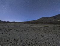 the stars are in the sky above a mountain and dirt area on the horizon are black rocks