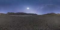 a view across an empty, rocky area under a starry sky over the horizon