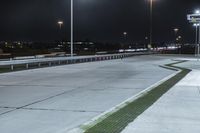 a road with lights on at night as a stop light watches from behind it and a freeway