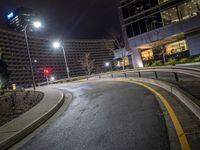 a curved, winding road at night in a city surrounded by tall buildings and a building on the other side