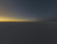 the sun is rising over an empty open space with tracks in the snow and one is walking