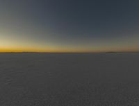 the sun is rising over an empty open space with tracks in the snow and one is walking