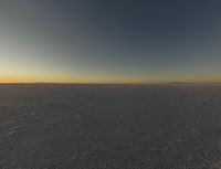 the sun is rising over an empty open space with tracks in the snow and one is walking