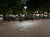 a night view of a street scene with bicycles parked on the pavement and the light in the dark above