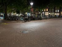 a night view of a street scene with bicycles parked on the pavement and the light in the dark above