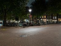 a night view of a street scene with bicycles parked on the pavement and the light in the dark above