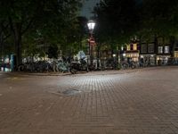 a night view of a street scene with bicycles parked on the pavement and the light in the dark above