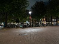 a night view of a street scene with bicycles parked on the pavement and the light in the dark above