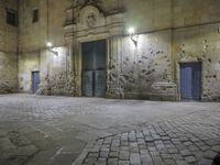 an empty stone sidewalk and building area with the lights on at night in the city