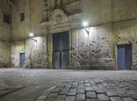 an empty stone sidewalk and building area with the lights on at night in the city