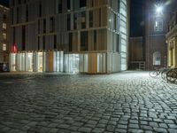 bicycle parked in a empty courtyard near a tall building at night, with the lights on