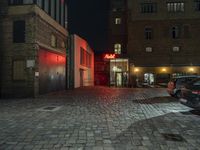 a street scene at night, with the car parked in front of a building and red light lit building