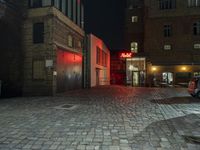 a street scene at night, with the car parked in front of a building and red light lit building