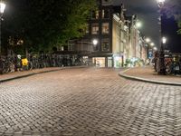 a group of bikes parked on side of a brick road at night with lights on