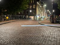 a group of bikes parked on side of a brick road at night with lights on