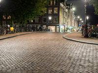 a group of bikes parked on side of a brick road at night with lights on