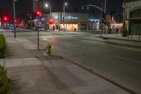 the fire hydrant in front of a store is lit up at night in an empty city