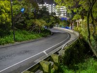 a road and roadway running under tall buildings on the hillside at night, viewed from a park