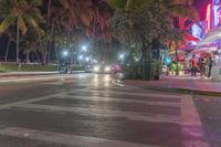 a crosswalk with some cars and palm trees at night on the side walk of the road
