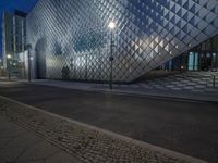 a street with stone sidewalks in front of a glassy building at night on the corner