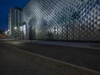 a street with stone sidewalks in front of a glassy building at night on the corner