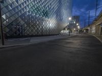 a street with stone sidewalks in front of a glassy building at night on the corner