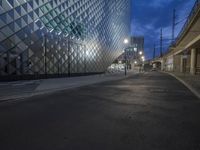 a street with stone sidewalks in front of a glassy building at night on the corner