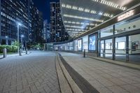 an empty sidewalk outside the building at night with lights reflecting on it's side