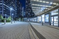 an empty sidewalk outside the building at night with lights reflecting on it's side