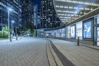 an empty sidewalk outside the building at night with lights reflecting on it's side