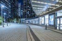 an empty sidewalk outside the building at night with lights reflecting on it's side