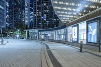 an empty sidewalk outside the building at night with lights reflecting on it's side