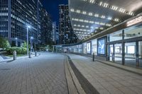 an empty sidewalk outside the building at night with lights reflecting on it's side