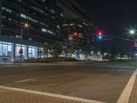 street with no traffic at night next to tall building and traffic lights on street corner