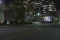 a night scene shows empty road in the distance in front of modern tall buildings in an urban city